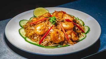 Fried shrimp with crispy salt and pepper served with coriander, lemon, red chili, and cucumber on a white plate over a jute mat. photo