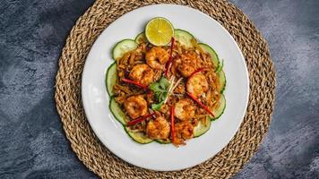 Fried shrimp with crispy salt and pepper served with coriander, lemon, red chili, and cucumber on a white plate over a jute mat. photo