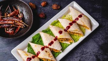 Royal Indian kathi rolls with spicy sauce and lettuce on a white plate., chilies on the side photo