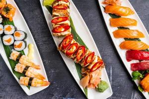 Plates filled with different types of sushi, Saki Sushi, Kraken Sushi, Salmon jhow sushi, Nigiri sushi, and Salmon hosomaki sushi on a black table. photo