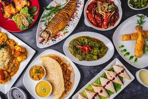 Nawabi Indian curry dishes with grilled fish, spicy chicken curry, paratha bajhi, prawn curry, biriyani, rolls, tomato, and green curry. photo