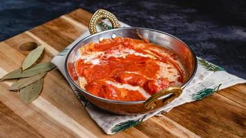 Butter chicken curry on a plank of wood and handmade mat, cinnamon leaves on the side. photo