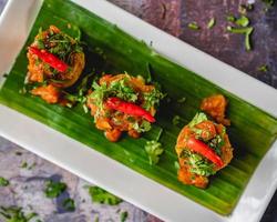 Fish kebabs with chili chutney served with red chili and coriander on a white plate with banana leaves. photo