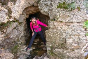 smiling woman hiker emerging from a cave in the mountain rocks photo