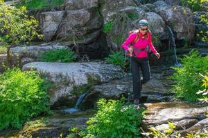 woman hiker crossing a river by the rocks photo