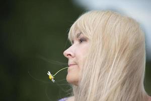 una mujer de mediana edad con el pelo blanco sostiene una flor de manzanilla en la boca. foto