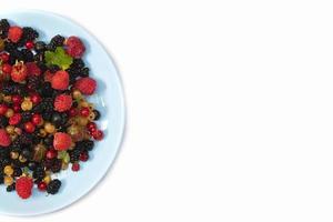 On a white background a plate with summer berries. Fruit salad with raspberries, gooseberries, currants, mulberries. Flat lay, top view photo