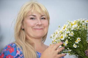 A beautiful plus size woman with white hair holds a bouquet of daisies, smiles, enjoys summer and life. photo