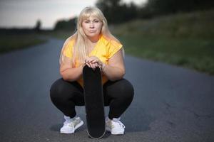 Chubby middle aged European woman, overweight, in a tracksuit with a skateboard, tired after playing sports, resting. photo