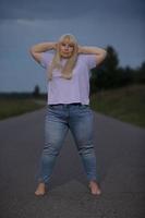 Plump middle aged woman posing in jeans on the street, overweight xxl. A full girl enjoys life. photo