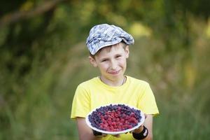 The boy is holding a plate of fruit. The child harvested in the garden. photo