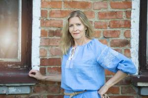 A beautiful elderly woman of Slavic appearance in an embroidered shirt against a brick wall. photo