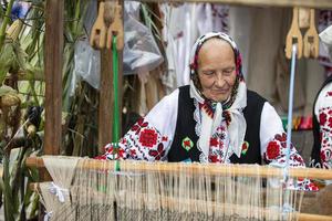 An old Belarusian or Ukrainian woman in an embroidered shirt at a vintage loom. Slavic elderly woman in national ethnic clothes. photo