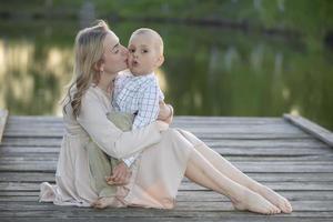Mom gently kisses her little son against the backdrop of nature. Maternal happiness. photo