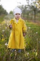 Child in the spring garden. Funny little girl in a yellow coat is holding dandelions. photo