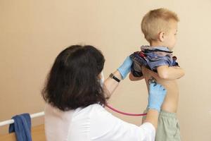 The doctor uses a stethoscope on the boy's back to check his health. photo
