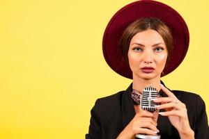 niña en un negro traje en un amarillo antecedentes canta en un retro micrófono, retrato, música foto