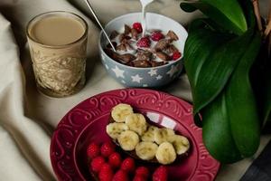 breakfast, cereal with milk, coffee with milk in a faceted glass, beterbrots with chocolate butter, berries and bananas photo