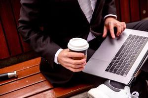 Young guy in a suit works on a computer in the park of a business center coffee in his hands photo