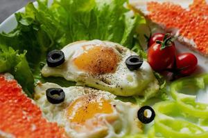 Breakfast, scrambled eggs on lettuce leaves, next to fresh vegetables and a sandwich with red caviar photo