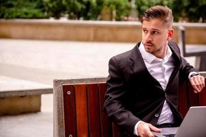 Young guy in a suit works on a computer in the park of a business center photo