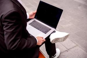 joven chico en un traje trabajos en un computadora en el parque, ordenador portátil cerca arriba foto