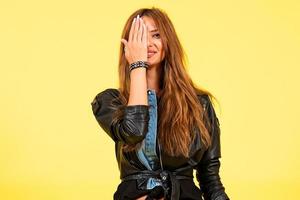 Yellow background, a girl in a leather jacket in the style of rock, shows emotions, free space for text, surprise photo