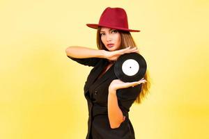 girl in a black suit on a yellow background with a record in her hands, music, the girl shows emotions photo