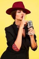 girl in a black suit on a yellow background sings in a retro microphone, portrait, music photo