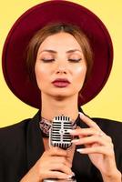 girl in a black suit on a yellow background sings in a retro microphone, portrait, music photo