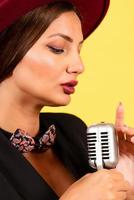 girl in a black suit on a yellow background sings in a retro microphone, portrait, music photo