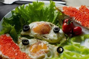 Breakfast, scrambled eggs on lettuce leaves, next to fresh vegetables and a sandwich with red caviar photo