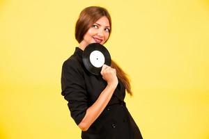 girl in a black suit on a yellow background with a record in her hands, music, the girl shows emotions photo