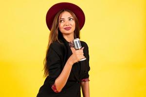 girl in a black suit on a yellow background sings in a retro microphone, portrait, music photo