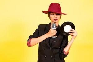 girl in a black suit on a yellow background sings in a retro microphone, portrait, music, full growth photo