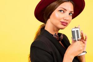 niña en un negro traje en un amarillo antecedentes canta en un retro micrófono, retrato, música foto