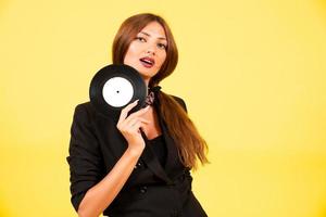 girl in a black suit on a yellow background with a record in her hands, music, the girl shows emotions photo