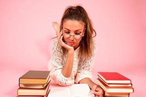 rosado fondo, un niña lee libros, un libro amante, un estudiante mentiras en el piso entre un grande número de libros foto