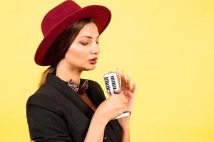 girl in a black suit on a yellow background sings in a retro microphone, portrait, music photo