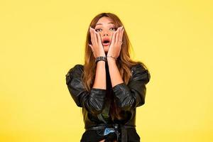 Yellow background, a girl in a leather jacket in the style of rock, shows emotions, free space for text, surprise photo