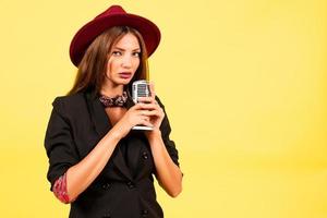 niña en un negro traje en un amarillo antecedentes canta en un retro micrófono, retrato, música foto