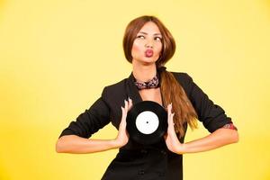 girl in a black suit on a yellow background with a record in her hands, music, the girl shows emotions photo