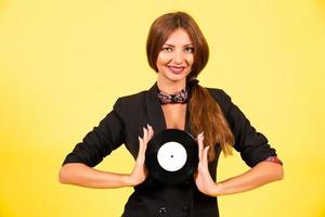 girl in a black suit on a yellow background with a record in her hands, music, the girl shows emotions photo