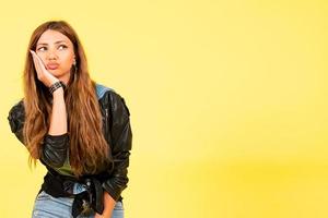 Yellow background, a girl in a leather jacket in the style of rock, shows emotions, free space for text, puffed out her cheeks photo