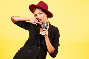 girl in a black suit on a yellow background sings in a retro microphone, portrait, music photo