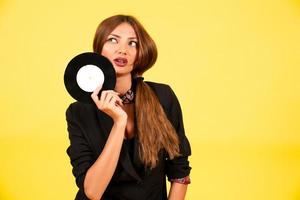 girl in a black suit on a yellow background with a record in her hands, music, the girl shows emotions photo