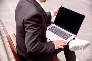 joven chico en un traje trabajos en un computadora en el parque, ordenador portátil cerca arriba foto