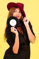 girl in a black suit on a yellow background with a record in her hands, music, the girl shows emotions photo