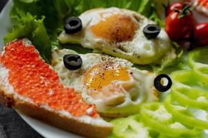 Breakfast, scrambled eggs on lettuce leaves, next to fresh vegetables and a sandwich with red caviar photo