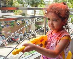 dulce pequeño indio niña jugando colores en holi festival, participación pichakaree lleno de colores, holi festival celebraciones en Delhi, India foto